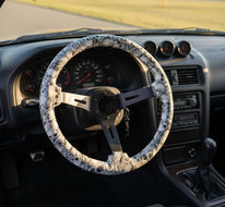 A three-spoke steering wheel with a white and black skull wrap on the rim and a dark metallic center, displayed against a black and white branded background.