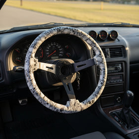 A three-spoke steering wheel with a white and black skull wrap on the rim and a dark metallic center, displayed against a black and white branded background.