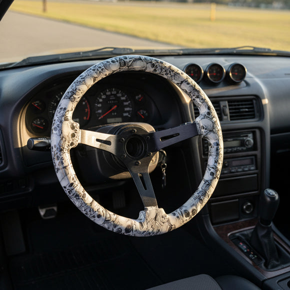 A three-spoke steering wheel with a white and black skull wrap on the rim and a dark metallic center, displayed against a black and white branded background.