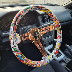 A steering wheel cover featuring a colorful comic book and graffiti print, wrapped around a bronze-colored spoke steering wheel, 