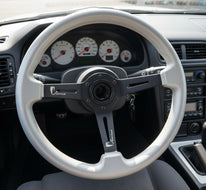 A silver steering wheel rim with a black three-spoke center, photographed from above on a dark wood surface.