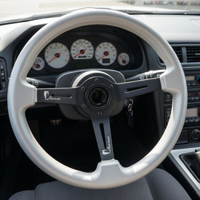 A silver steering wheel rim with a black three-spoke center, photographed from above on a dark wood surface.