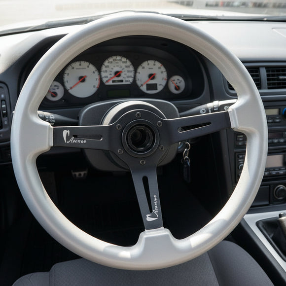 A silver steering wheel rim with a black three-spoke center, photographed from above on a dark wood surface.